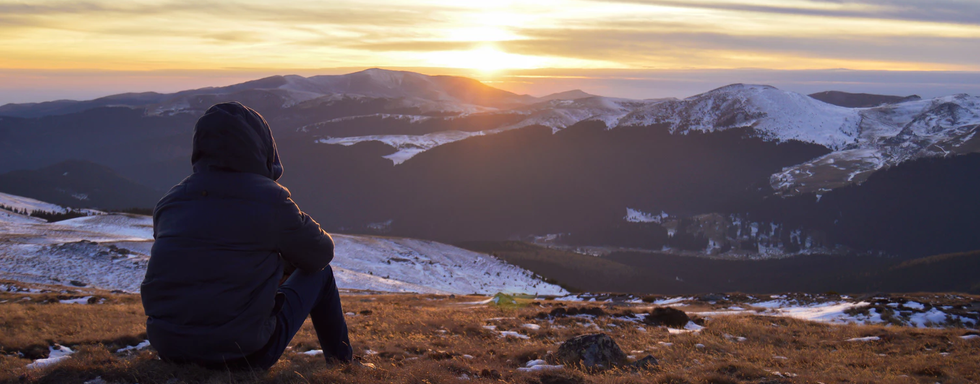 Persona sentada viendo el amanecer entre montañas