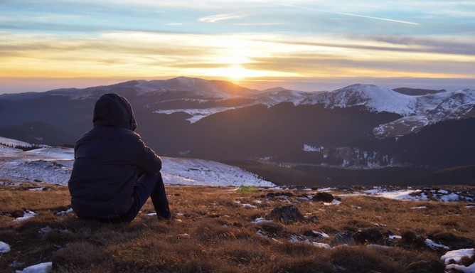 Persona sentada viendo el amanecer entre montañas